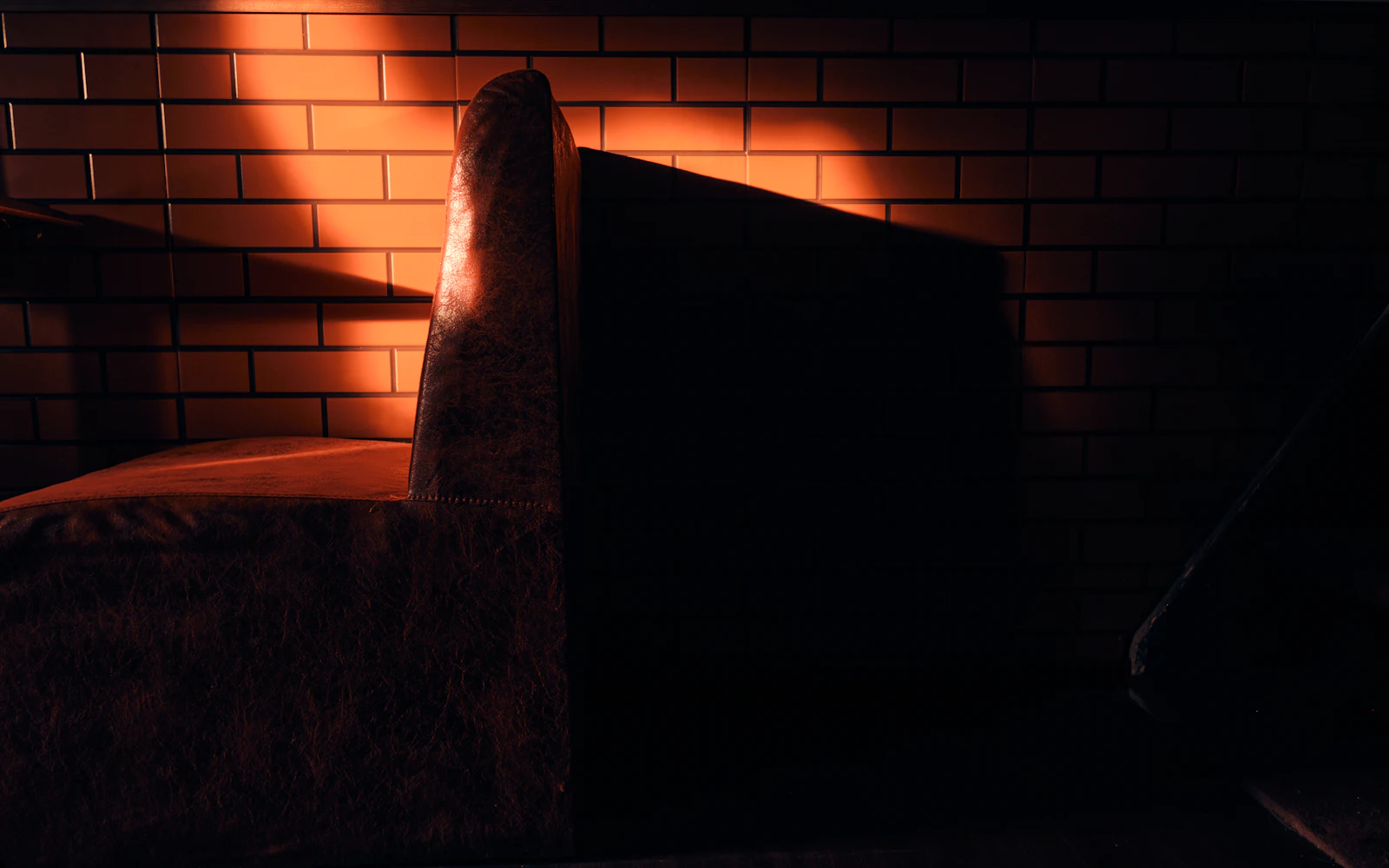 Sillón de cuero contra una pared de ladrillo, iluminado por una luz cálida